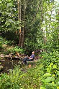 An adult is sitting at Oliver creekside in a chair meditating.